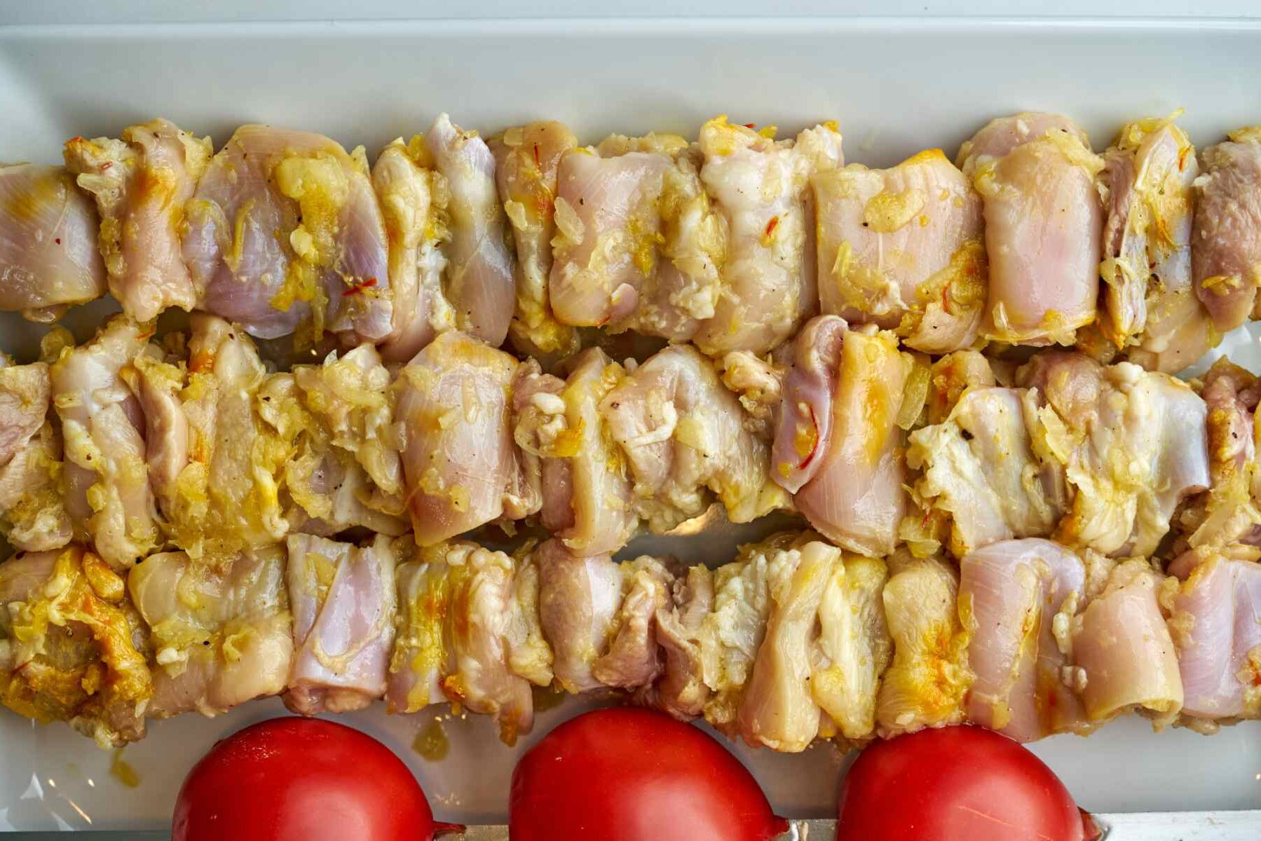 Raw chicken kabobs next to tomatoes.