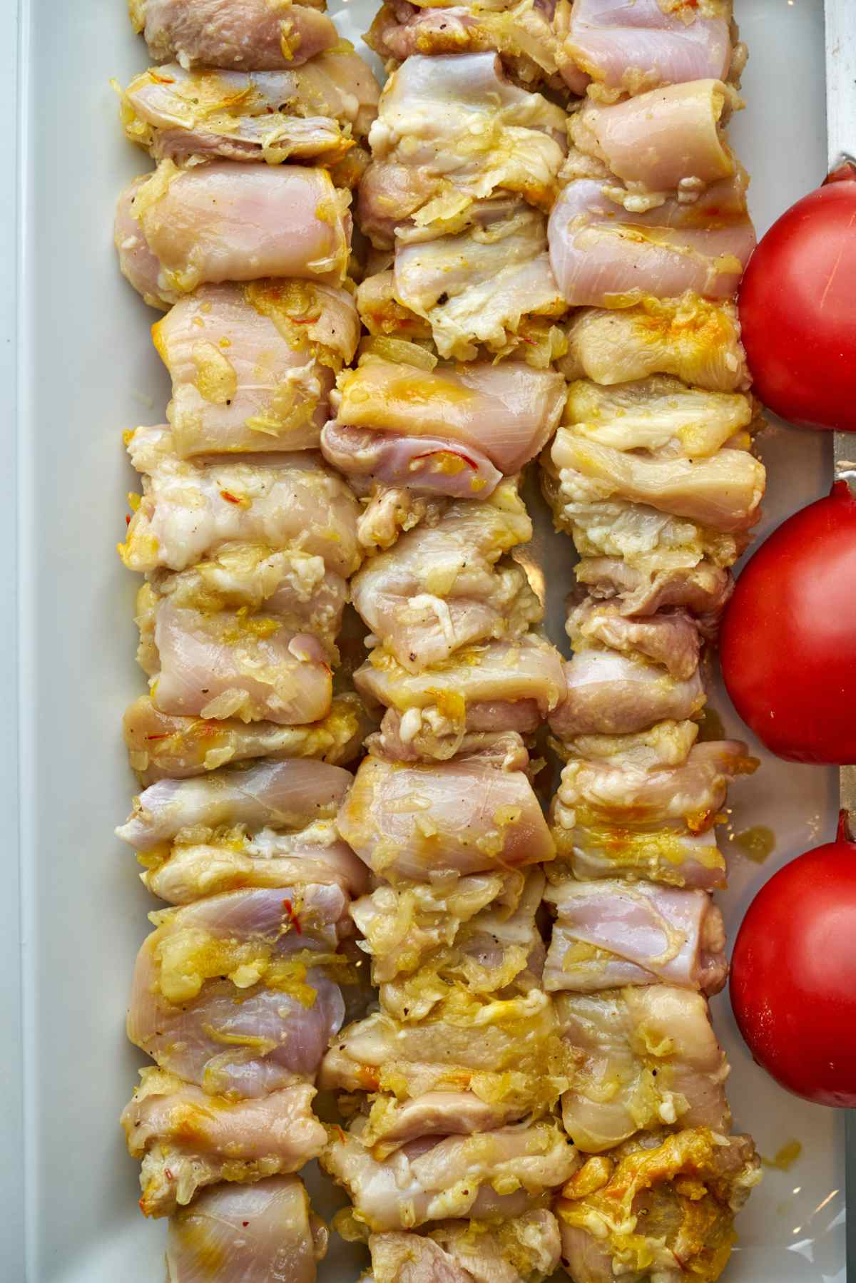 Raw chicken kabobs next to tomatoes.