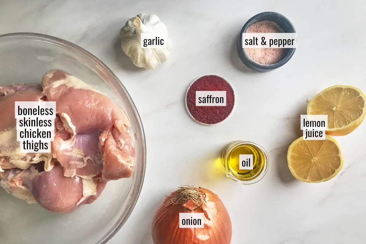 Ingredients to make chicken kabobs like saffron, onion, boneless chicken, and a lemon on a countertop.