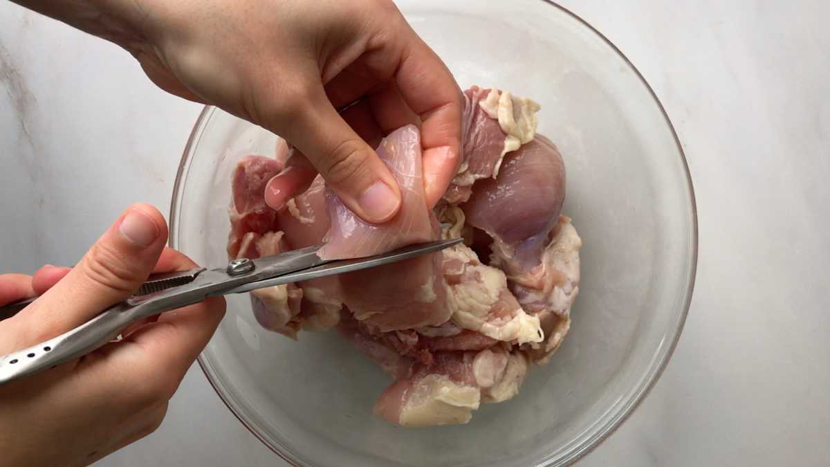 Cutting raw chicken in a bowl.