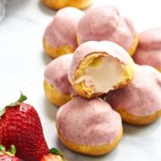 Stack of pink cream puffs next to strawberries.