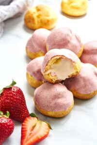 Stack of pink cream puffs next to strawberries.