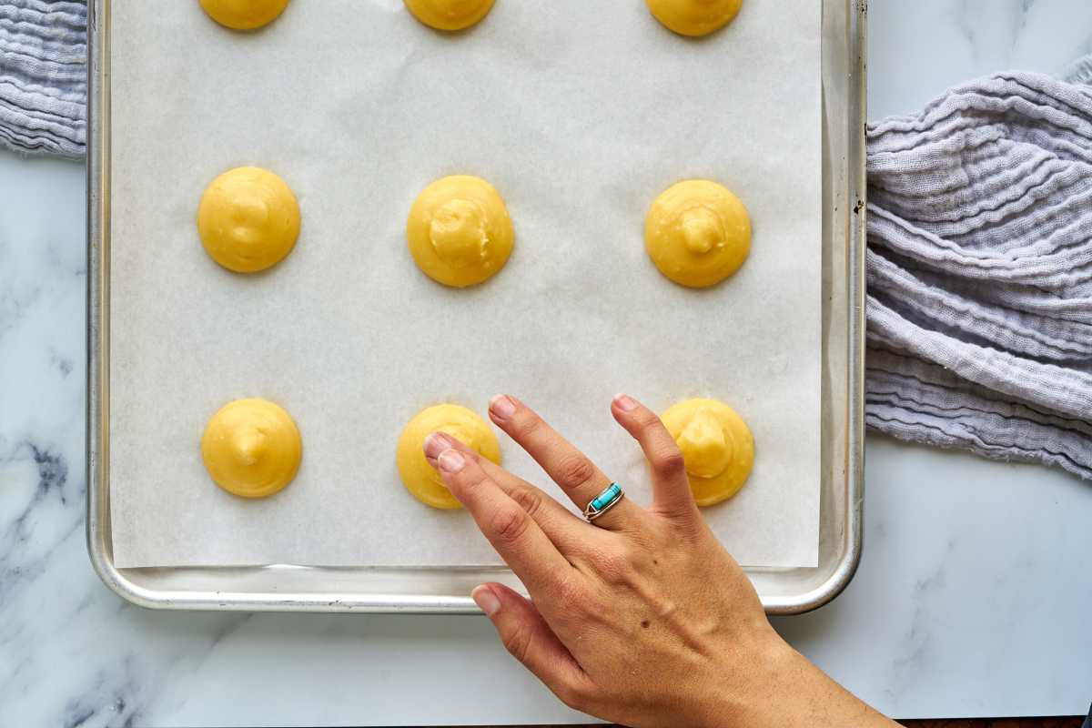 Smoothing the tops of raw choux dough with a finger.