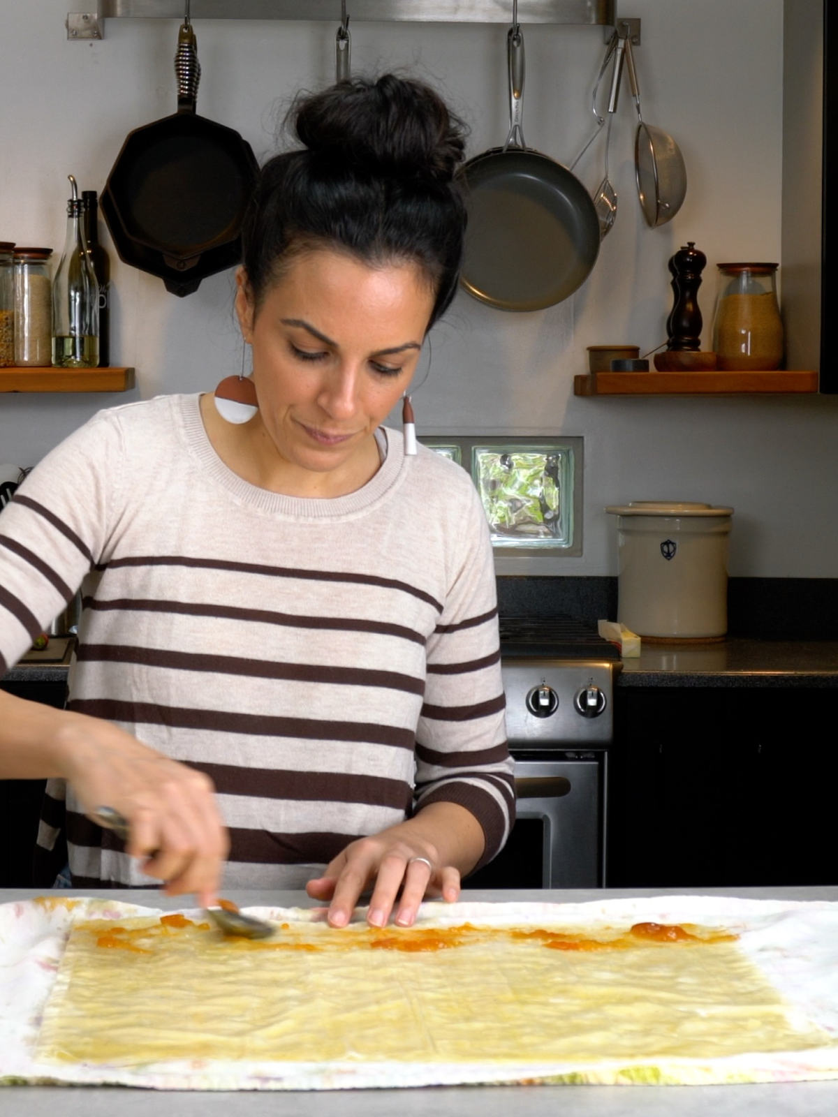 Woman in a stripy shirt smearing apricot jam on a stack of phyllo dough.