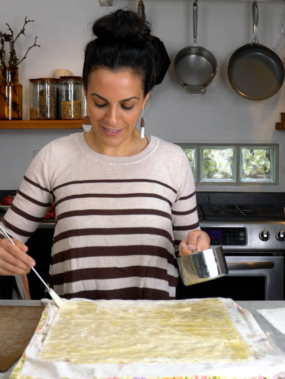 A woman in a stripy shirt brushing layered phyllo dough with butter.