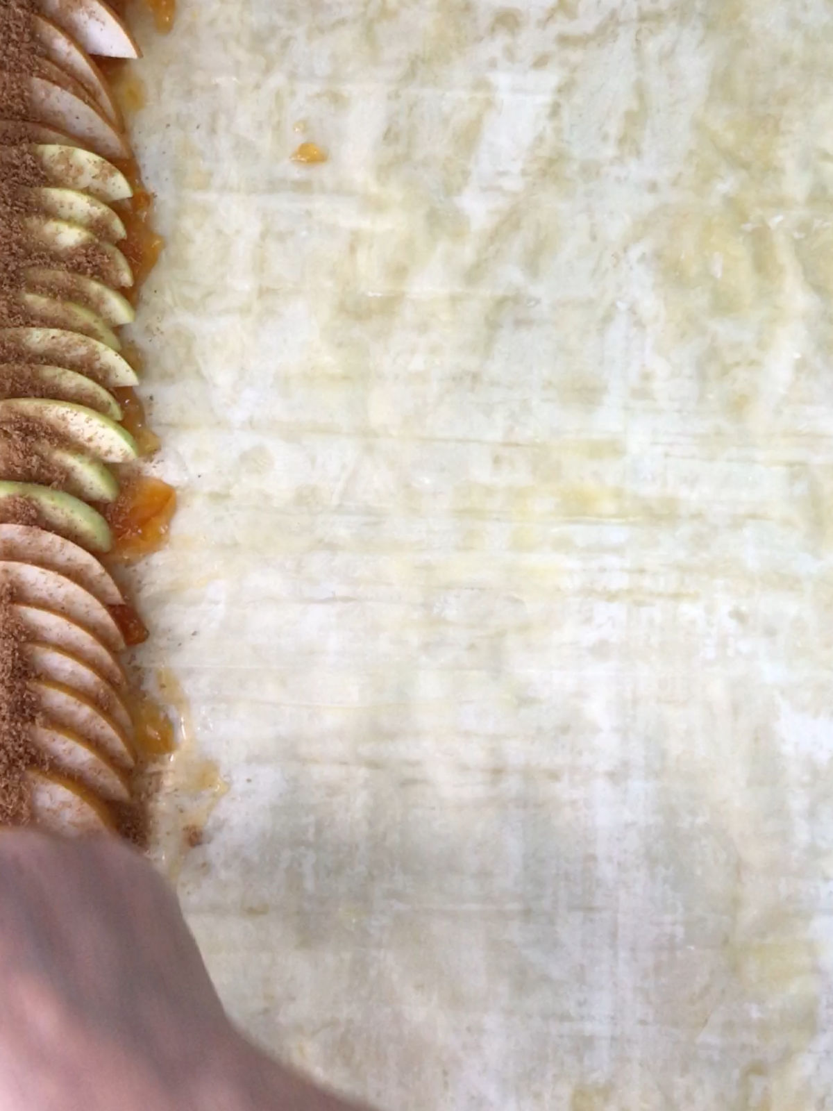 A hand sprinkling cinnamon sugar on a stack of neat apples on one side of phyllo dough.