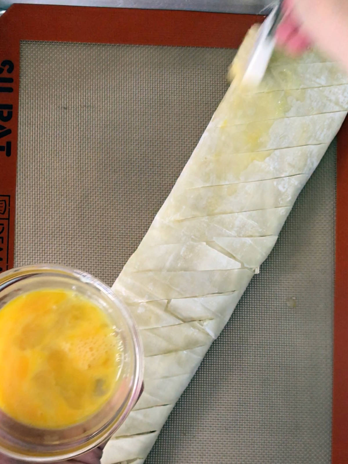 A hand in motion brushing egg wash on a phyllo pastry log.