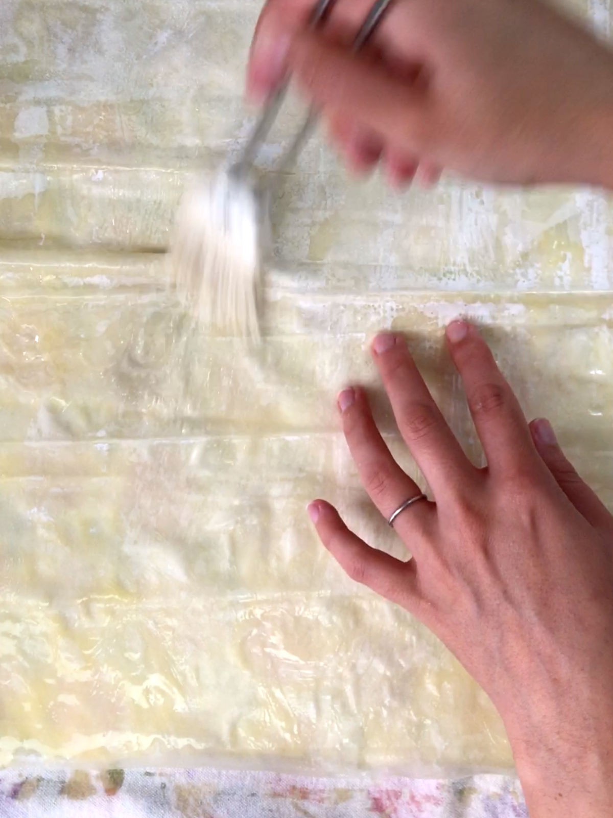 Two hands brushing phyllo dough with butter with a white silicone brush.