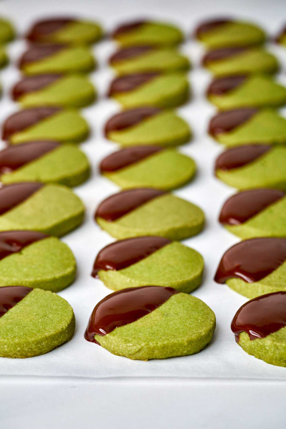 Rows of round green cookies dipped diagonally in dark chocolate.