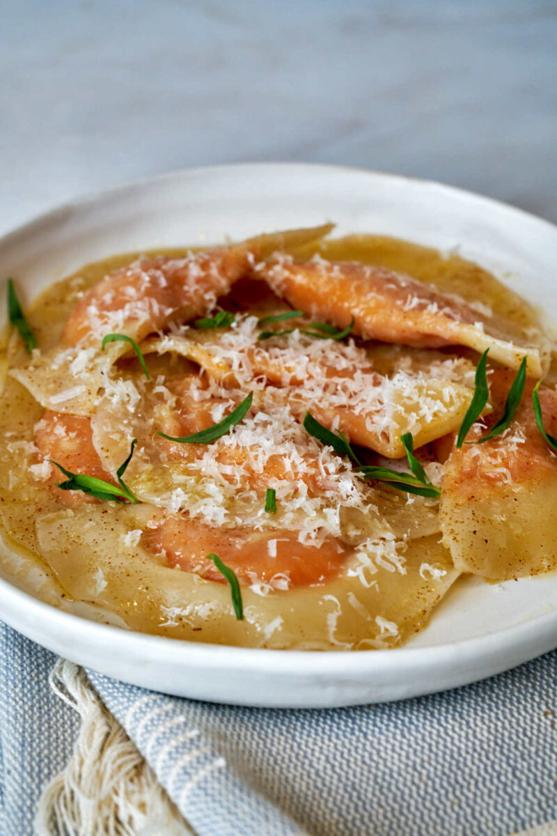 Orange ravioli on a plate with fresh herbs.