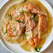 Orange ravioli on a plate with fresh herbs.