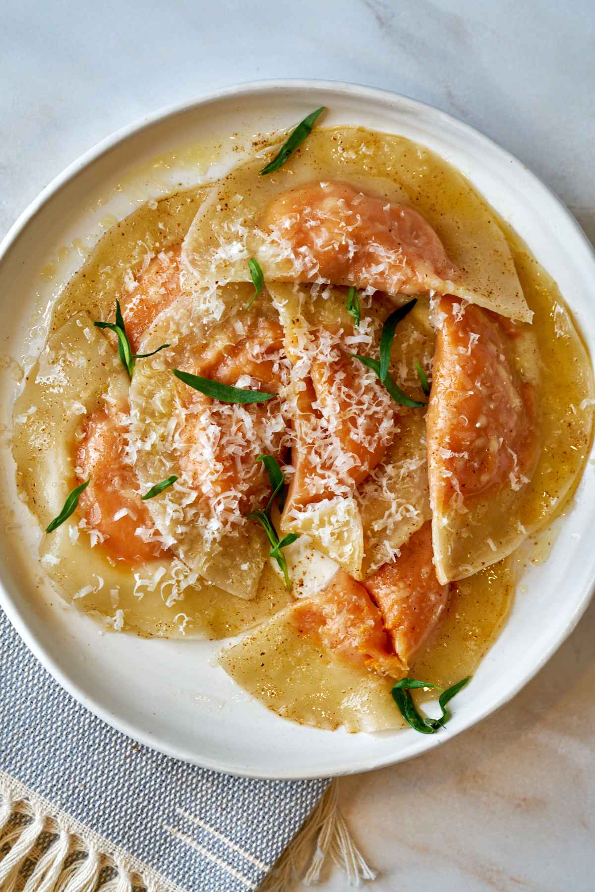 Orange ravioli on a plate with fresh herbs.