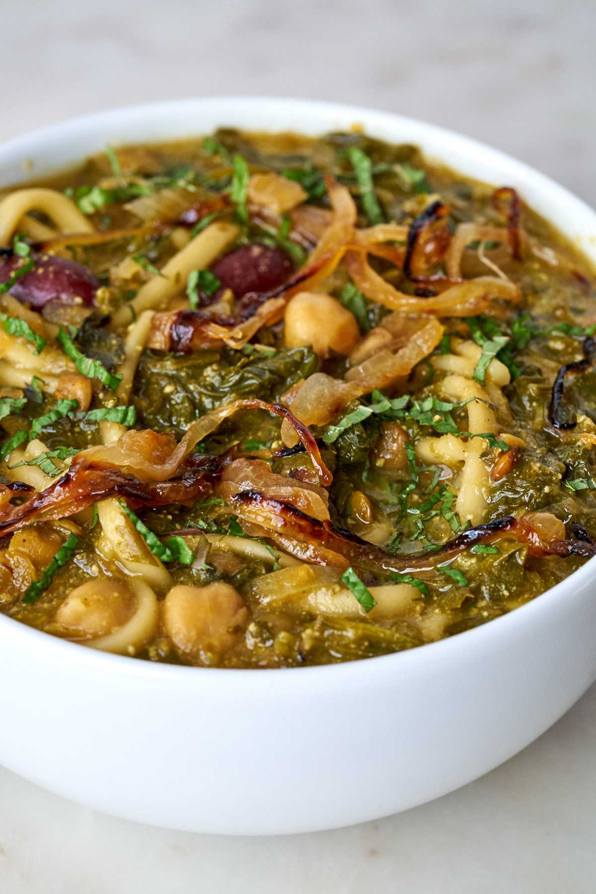 Bowl of green soup with noodles and beans.