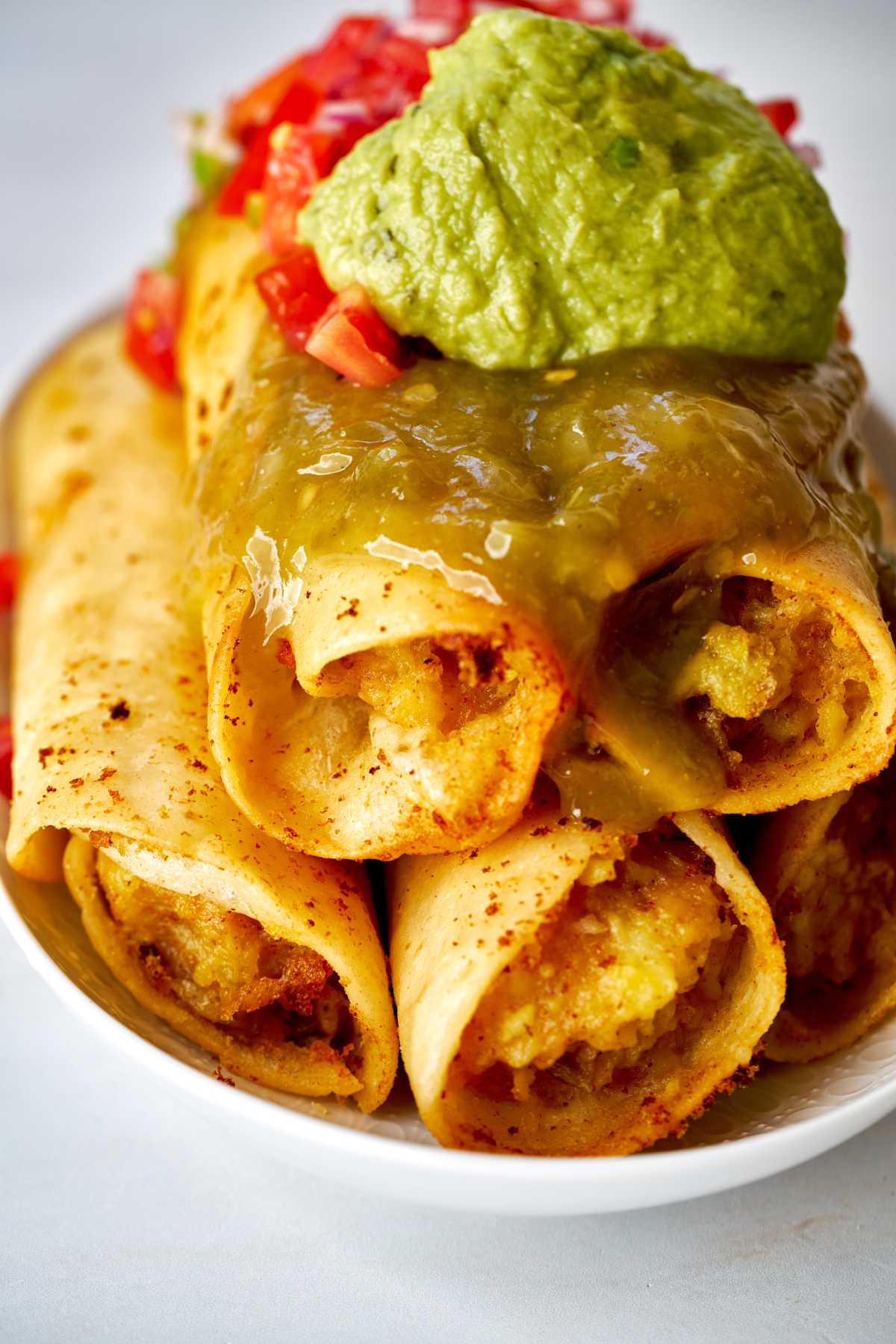 A stack of rolled tacos with guacamole and salsa.