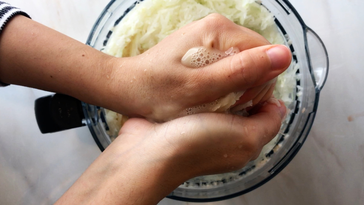 Hands squeezing liquid out of shredded potatoes.