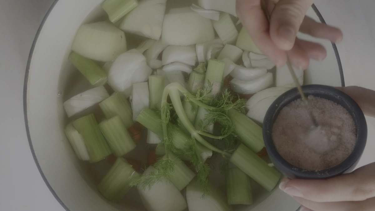 Adding salt to vegetables in a soup pot.