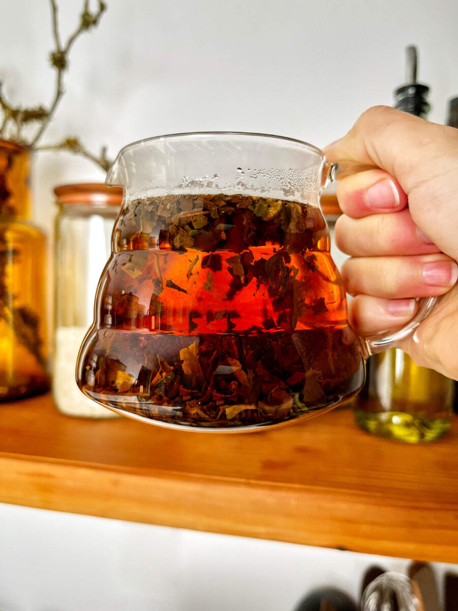 Brewed tea in a glass teapot above a wood floating shelf.