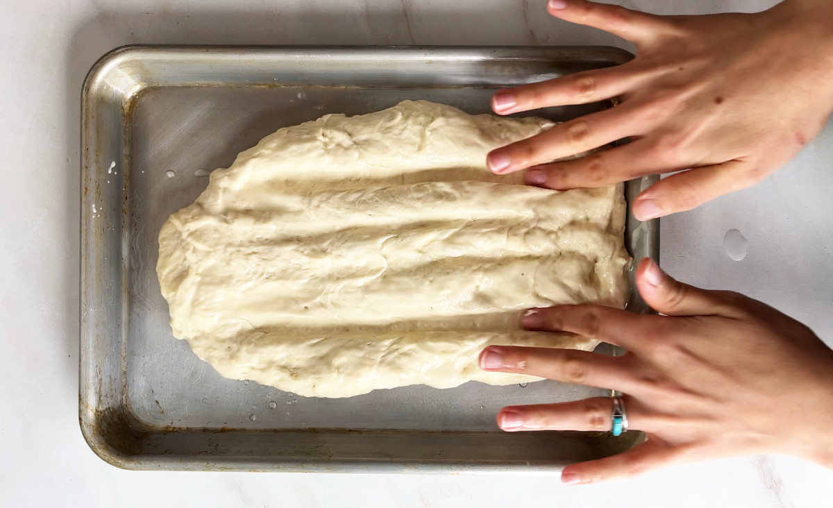 Fingers making grooves in dough on a baking sheet.