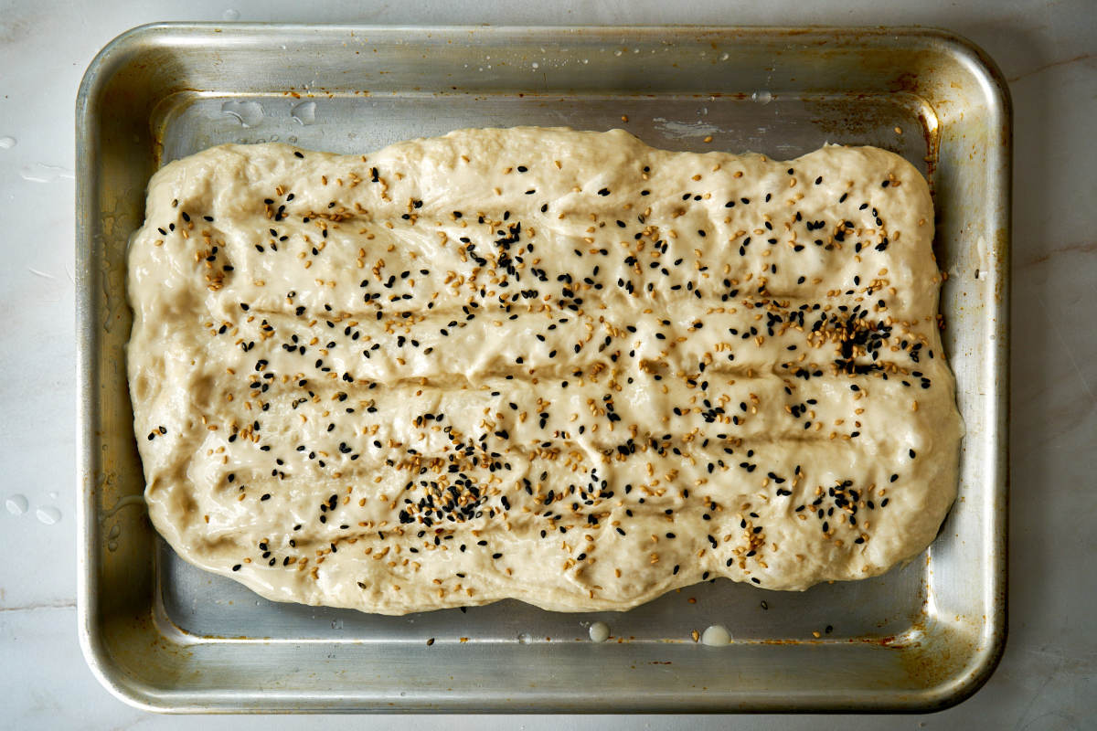 Dough with sesame seeds on a baking sheet.