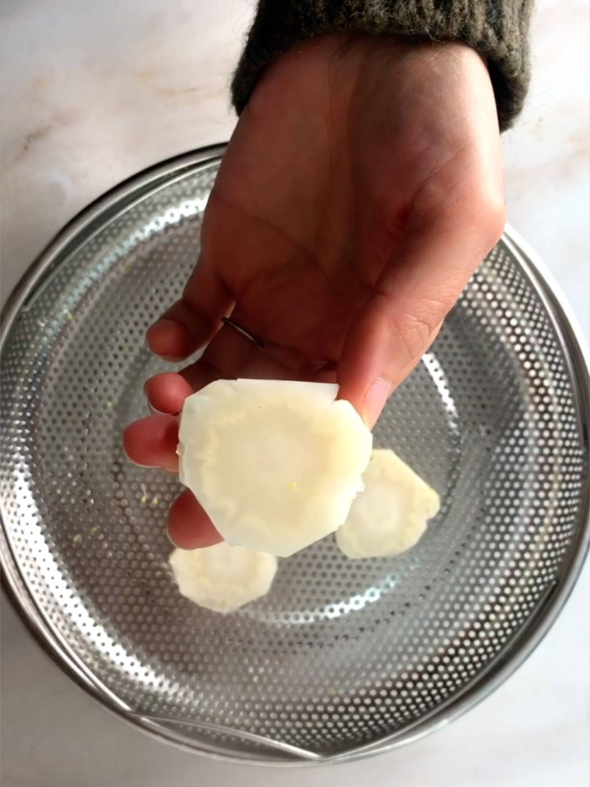 A hand holding a steamed disc of cauliflower over a steamer basket.