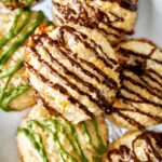 Cookies drizzled with chocolate stacked in a dish.