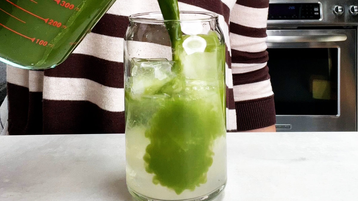 Green tea pouring into a glass of water and ice.
