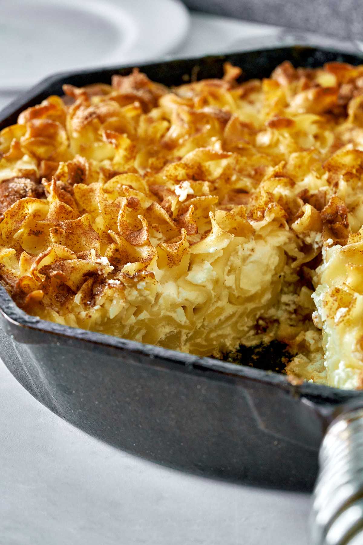 Baked noodle casserole with cinnamon topping in a cast iron pan.