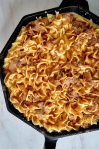 Baked noodle casserole with cinnamon topping in a cast iron pan.