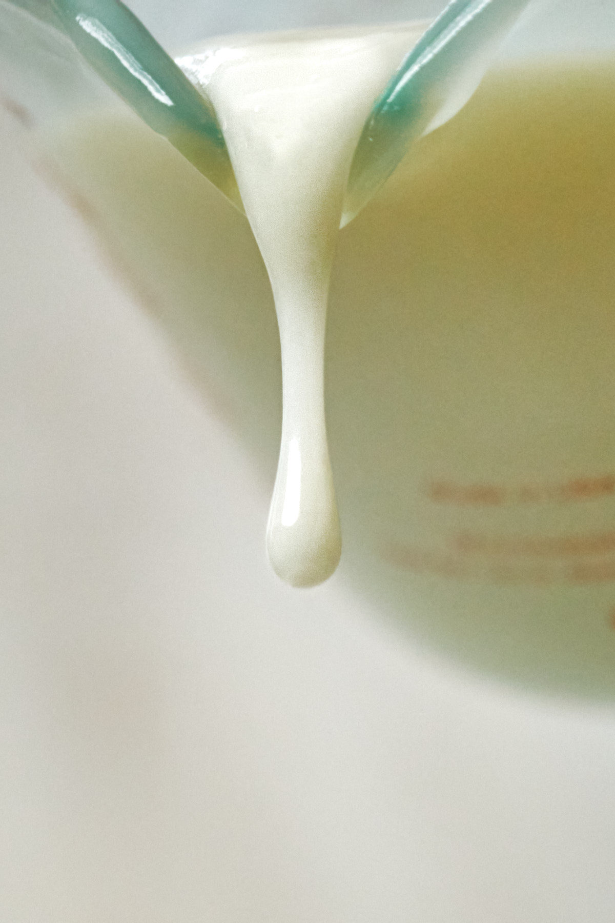 Drop of creamy liquid pouring out of a measuring cup.