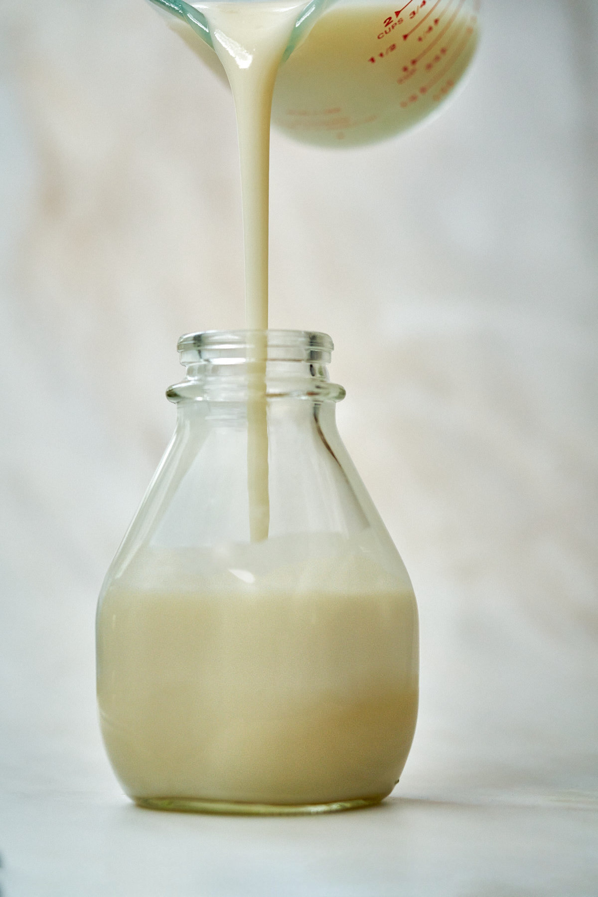 Pouring thick creamy liquid into a glass bottle.