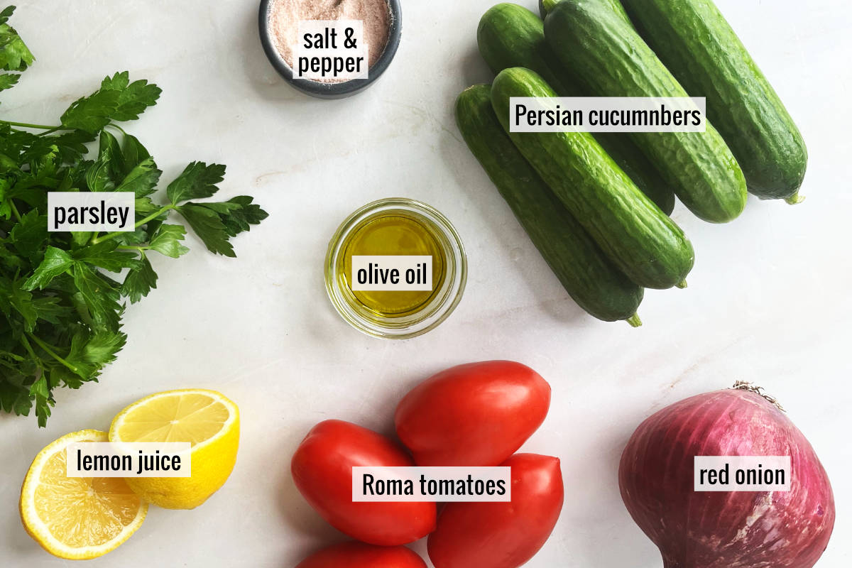 Cucumbers, tomatoes, lemon and other salad ingredients on a countertop.