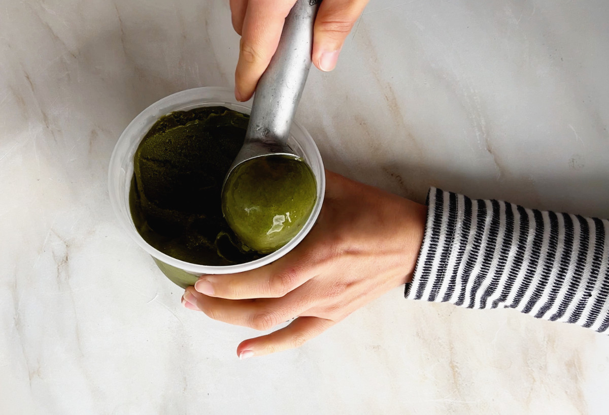 Scooping green nice cream from a plastic container.