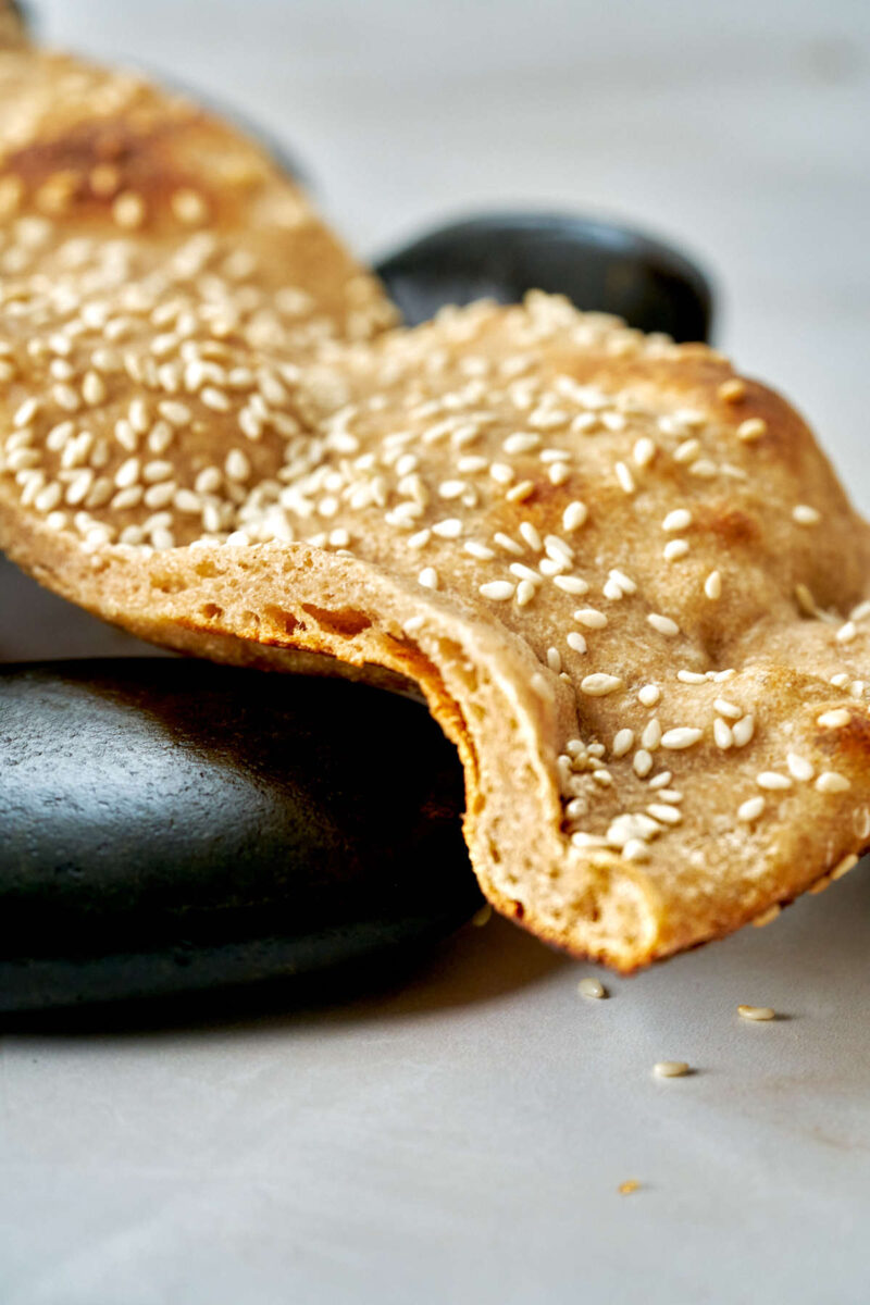 Flatbread with sesame seeds on black rocks.