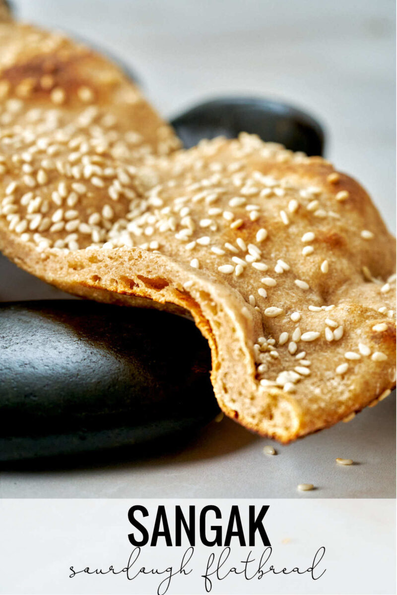 Flatbread with sesame seeds on black rocks and text.