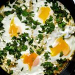 Eggs in a cast iron pan with green tomato sauce and cilantro.