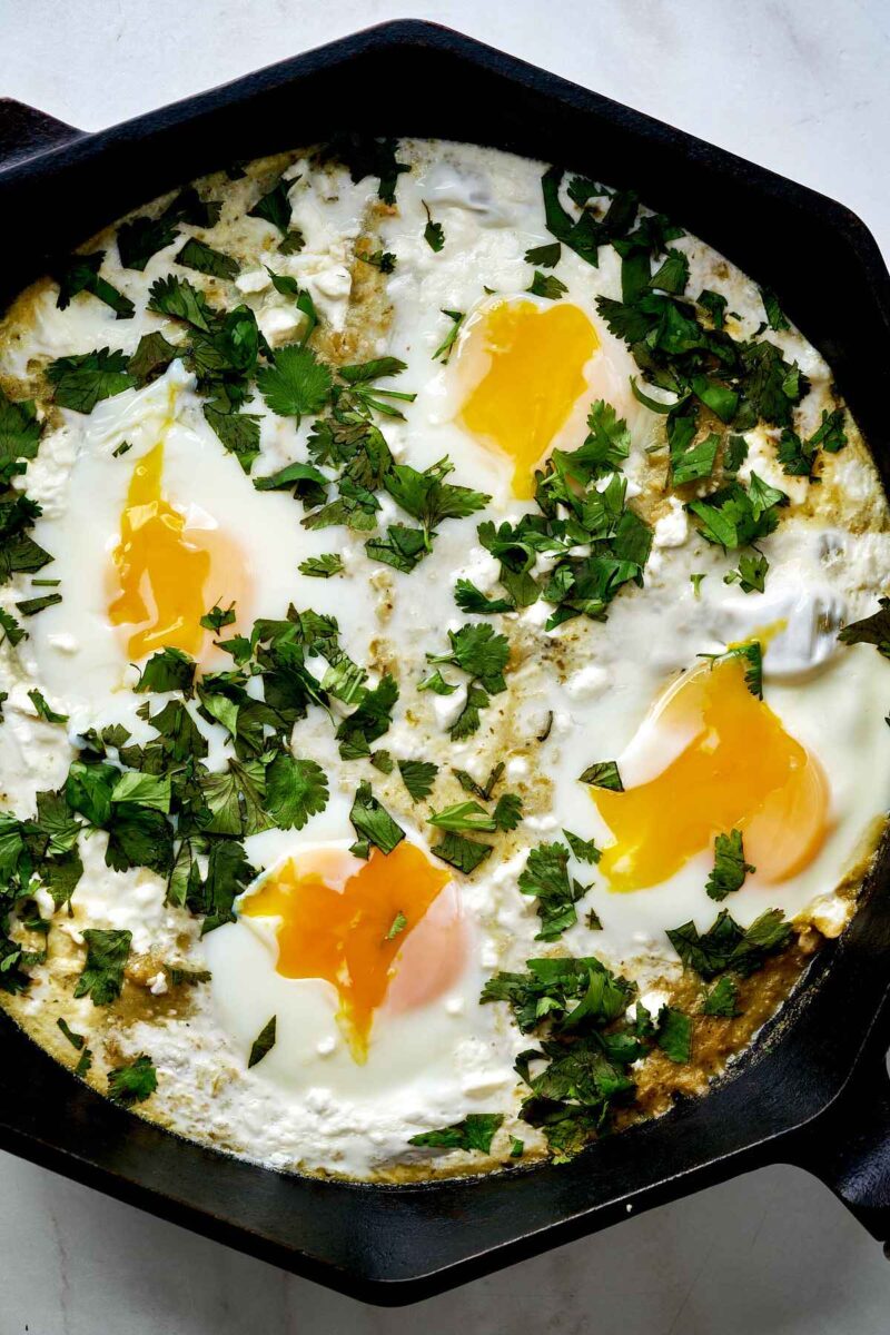 Eggs in a cast iron pan with green tomato sauce and cilantro.