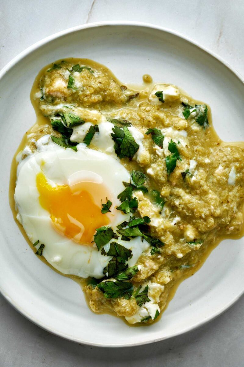 Eggs and green salsa on a white plate with cilantro.