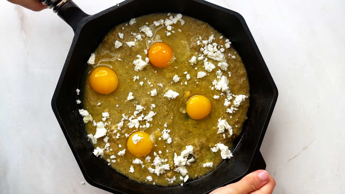 Green salsa with raw eggs in a cast iron pan.