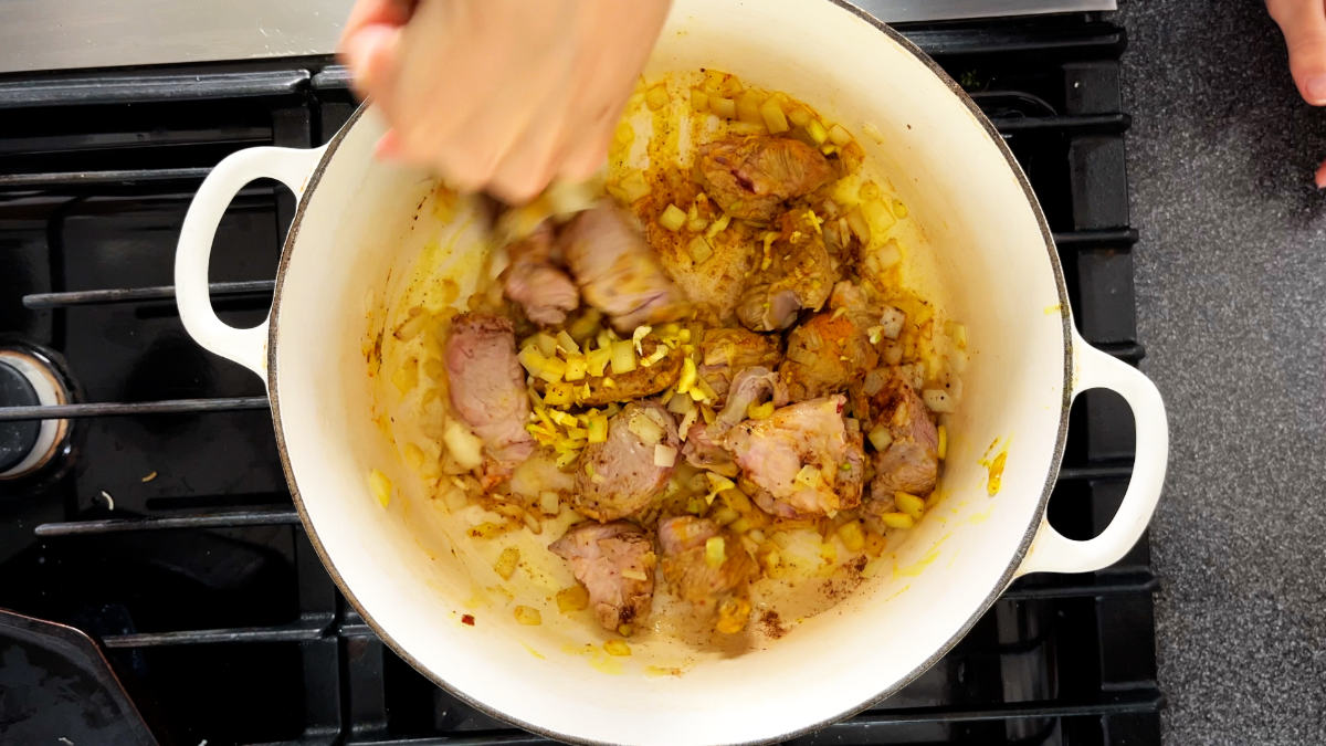 Meat browning in a white pot on a stove.