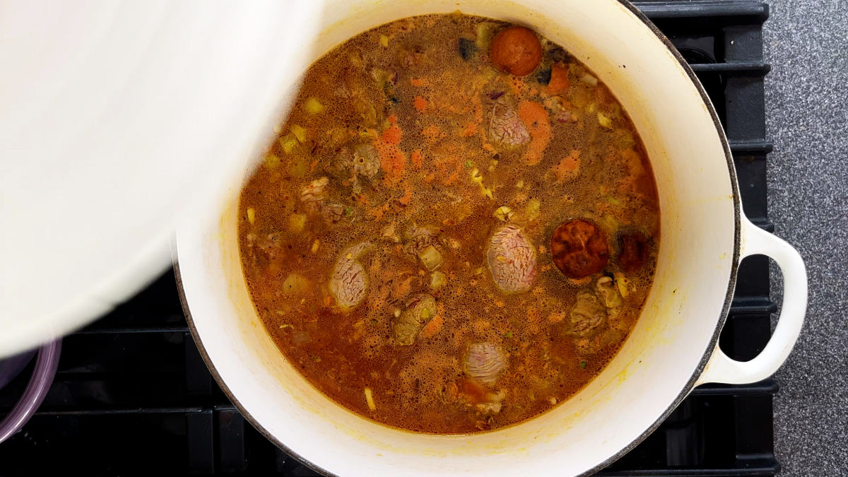 White pot on a stove with red stew.