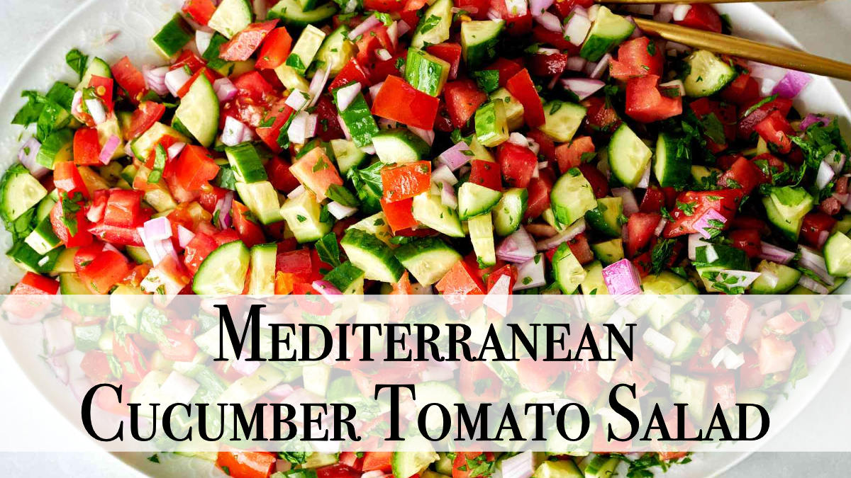 A top-down, close-up view of a large bowl of Mediterranean cucumber tomato salad. The salad is a vibrant mix of diced red tomatoes, dark green cucumbers, and finely chopped red onion and herbs. The vegetables are roughly equal in size and scattered throughout the bowl. Some gold-colored tongs rest on the side of the white bowl. Text is overlaid on the image that reads "Mediterranean Cucumber Tomato Salad".