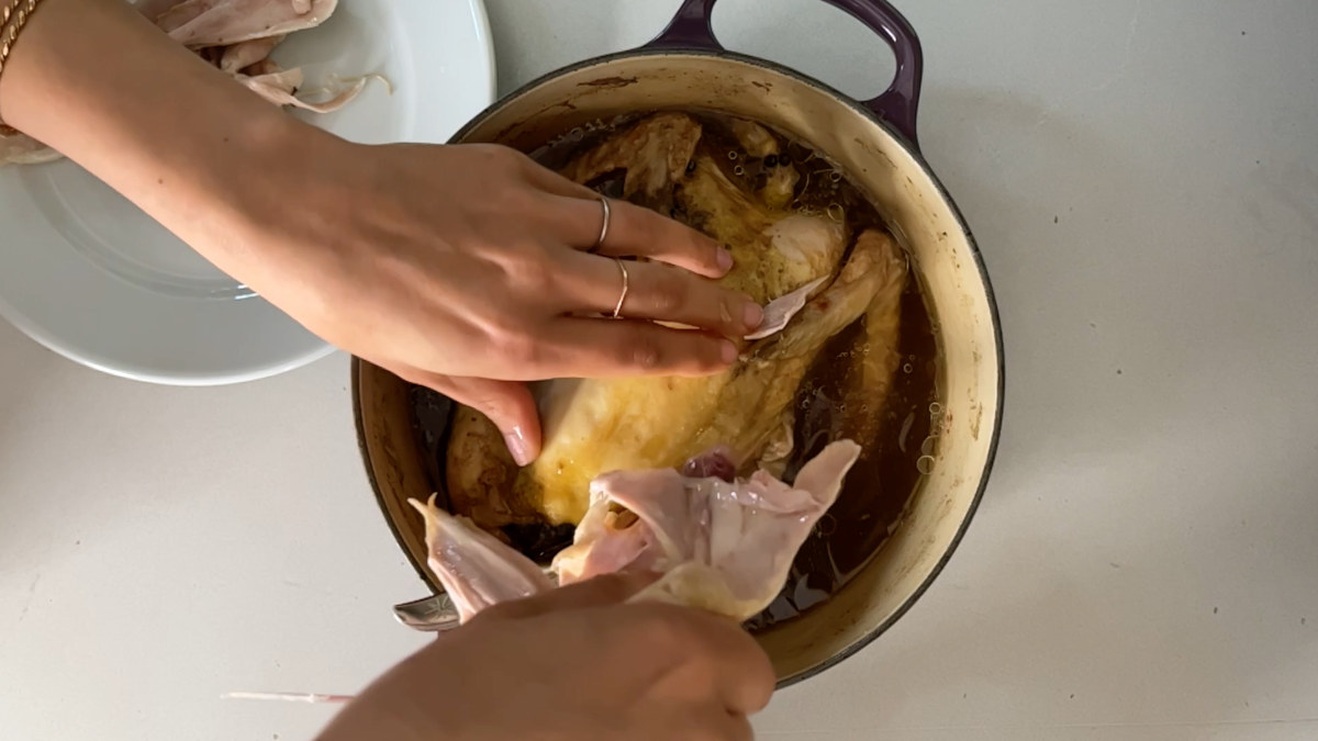 Hands deboning a chicken in a pot.