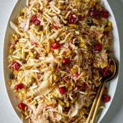 Rice with cherries and nuts on a white serving platter with gold serving spoons.