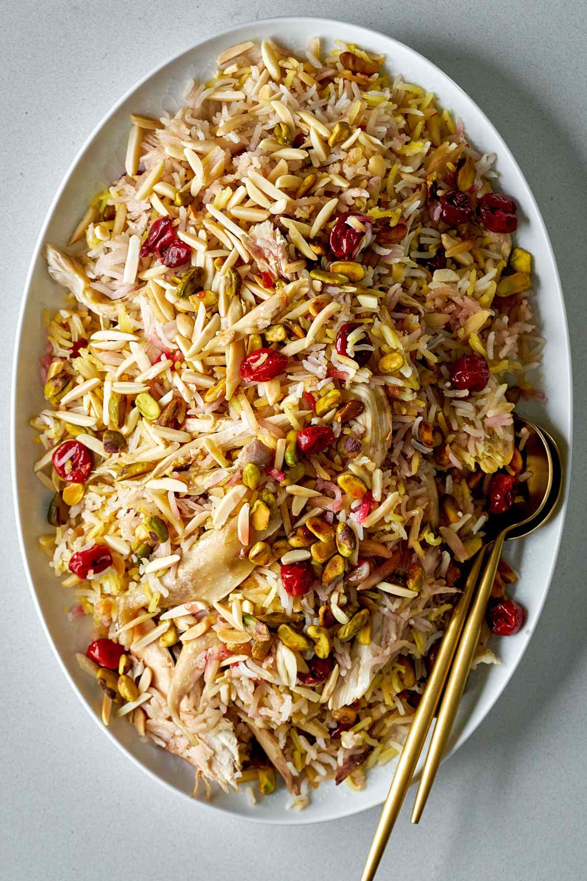 Rice with cherries and nuts on a white serving platter with gold serving spoons.