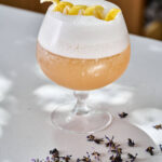 Peach mocktail with foam and lemon twist next to dried flowers.