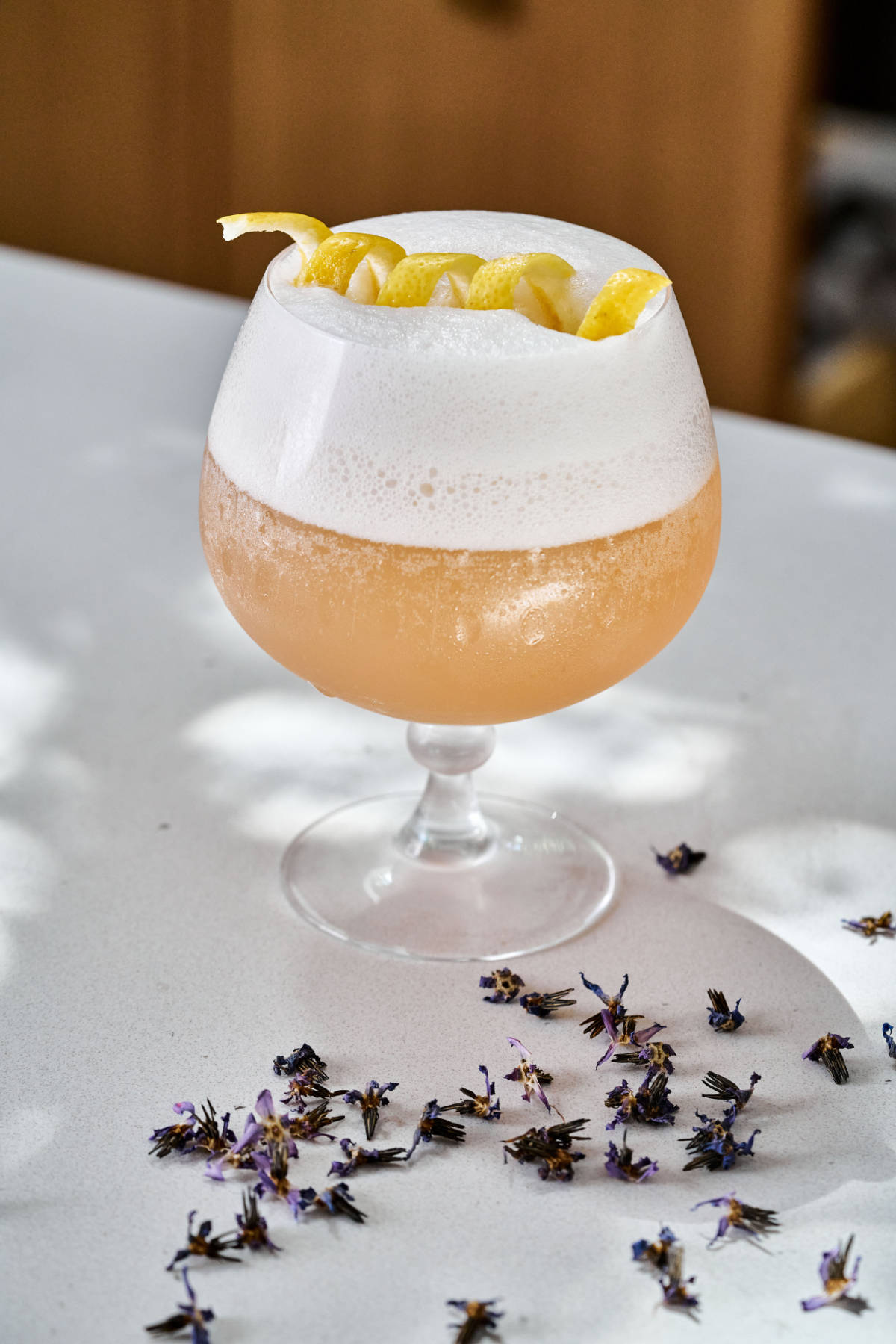 Peach mocktail with foam and lemon twist next to dried flowers.