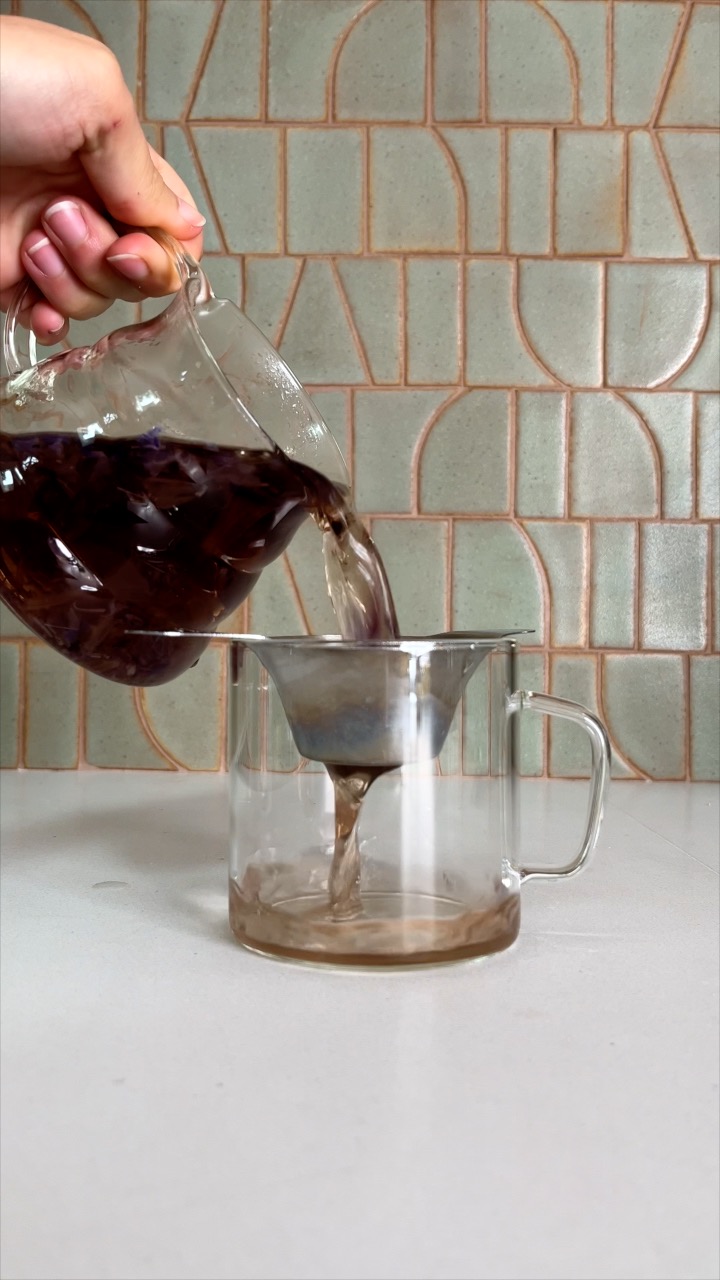 Straining steeped tea into a glass teacup.