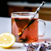 Glass of tea next to lemon and purple flowers.