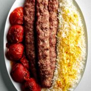 Meat kabobs on a plate with tomatoes and rice.