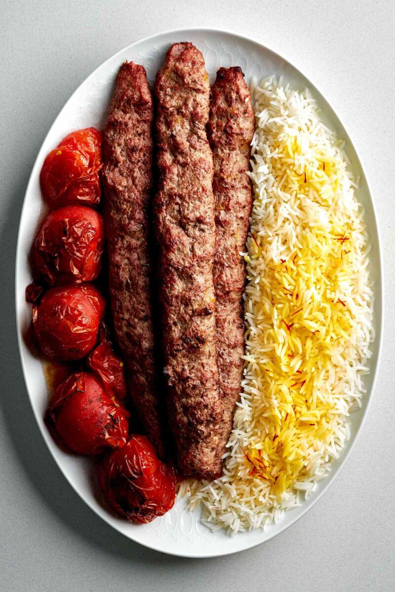 Meat kabobs on a plate with tomatoes and rice.